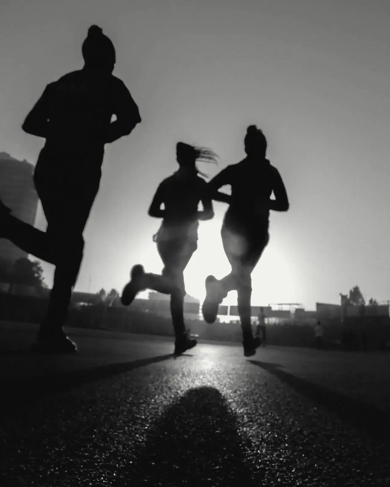 Three runners in silhouette against a low sun on an empty road.