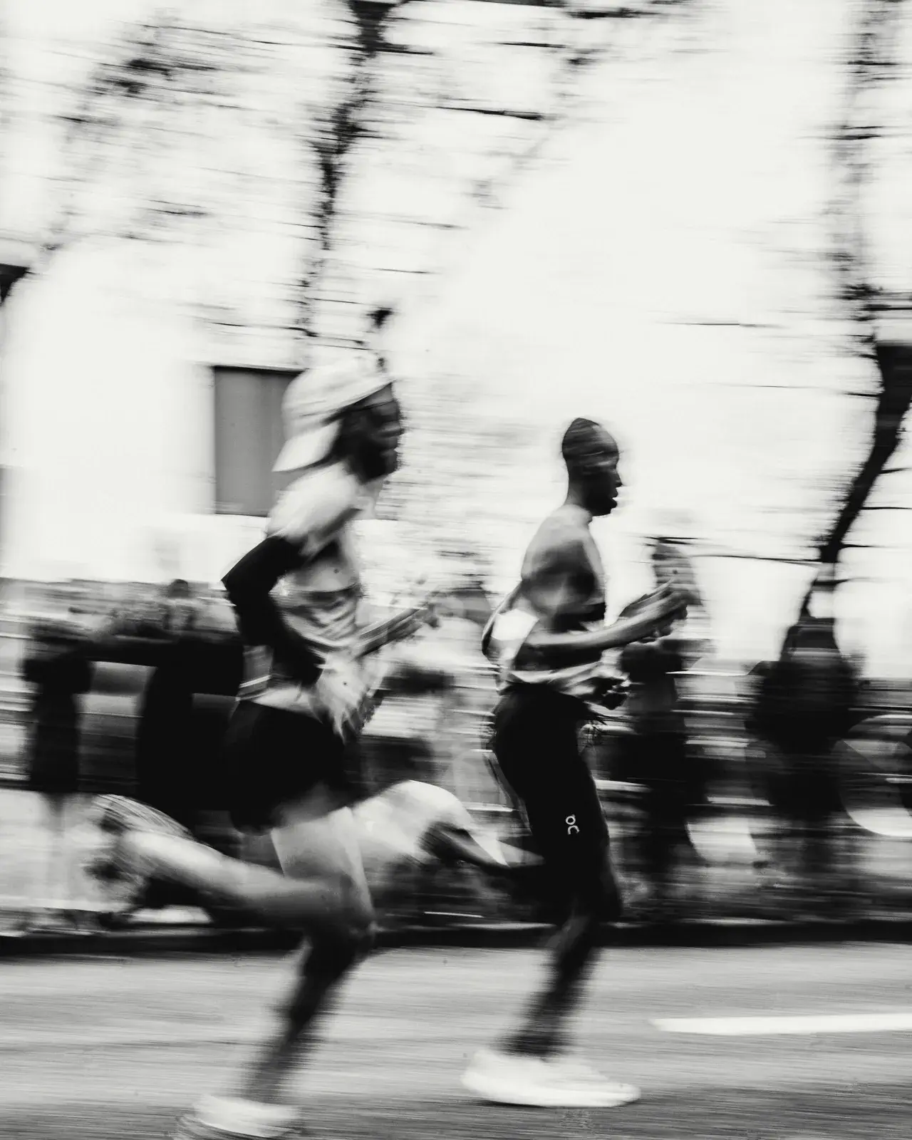 Two runners in motion blur on a city street, bare trees behind them.
